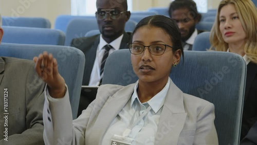 Young businesswoman in formalwear listening to speaker, taking notes and asking questions during professional conference