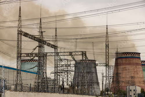 Cooling towers or chimneys of a coal fired power plant with pylons, wires and emissions; chimneys emitting pollution and greenhouse gases from a fossil fuel power station.