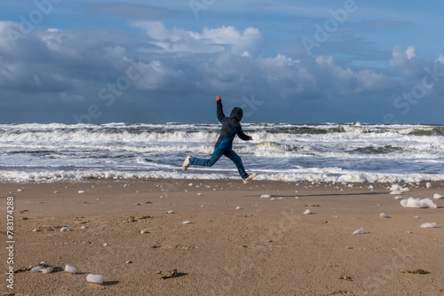 Ausgelassener Junge an einem Strand an der Nordsee an einem sonnigen und stürmischen Tag