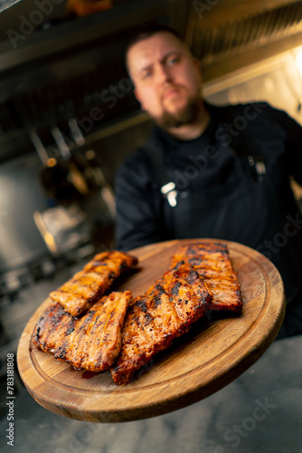in a professional kitchen the chef holds a board with ribs and demonstrates looking at the camera