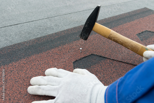 Close-up of a worker's hand hammering a nail into the soft roof of the roof
