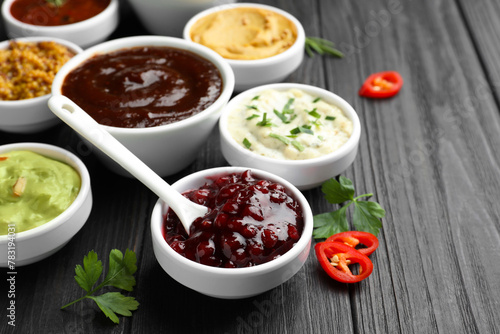 Different tasty sauces in bowls, parsley and chili pepper on black wooden table, closeup
