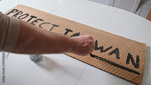 Caucasian Male Anti War Activist Preparing Banner for Political Demonstration Raid with Protect Taiwan Text Painted on Cardboard photo