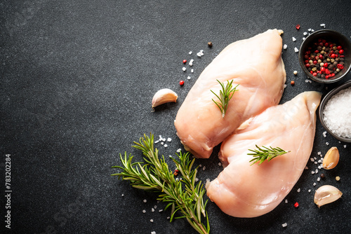 Uncooked chicken breast with spices at black table. Flat lay with copy space.