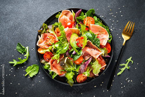 Healthy food. Fresh salad with jamon, green salad leaves and tomatoes. Top view with space for text. © nadianb