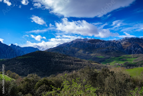 the towering Urriellu Mountain amidst vast valleys in the Picos de Europa mountain range. The rugged terrain is filled with lush greenery  rocky cliffs 