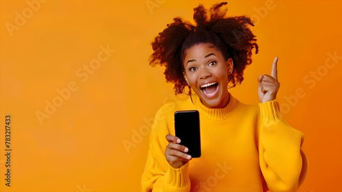 Excited young woman in yellow sweater with smartphone pointing upward. Casual, lifestyle, modern tech user. AI