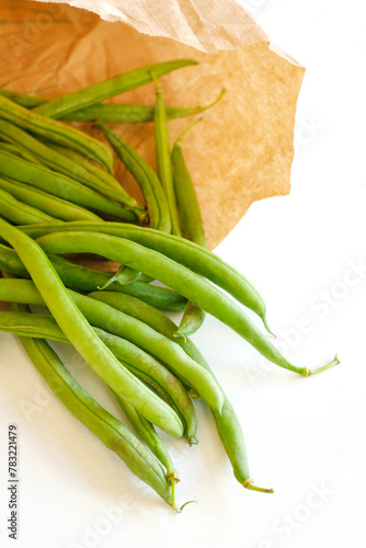 Closeup of organic ripe green bean pods in a brown paper eco bag on a white background. Zero waste environment concept.