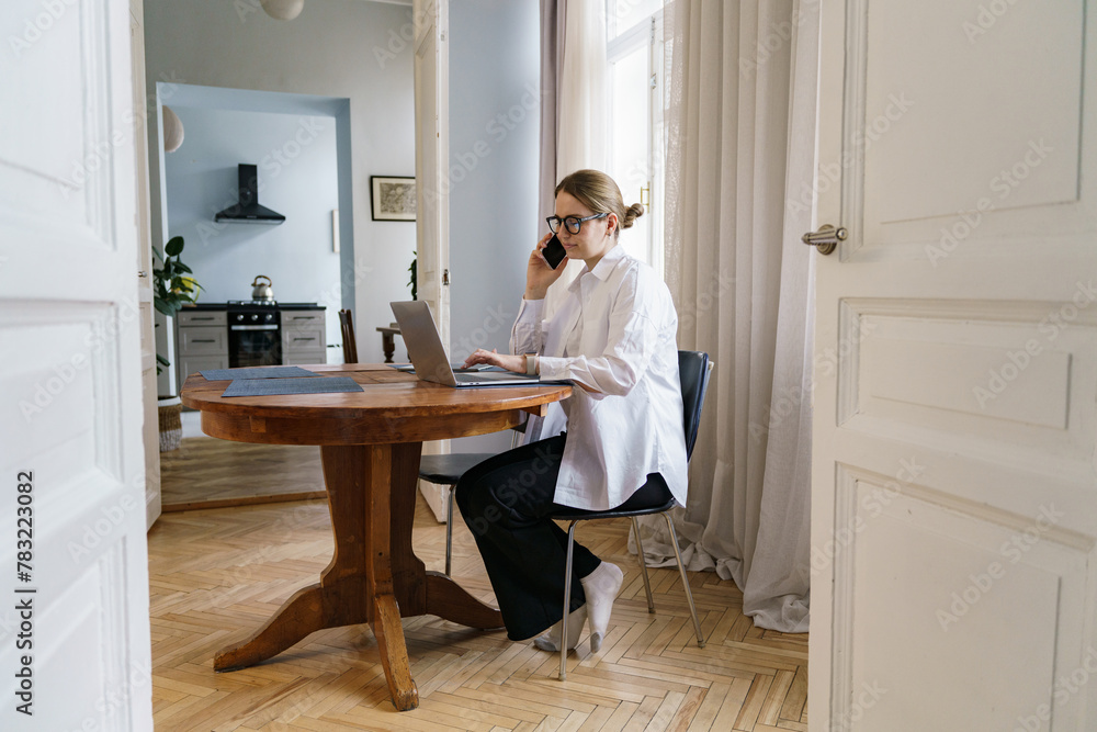A professional woman multitasks with a phone and laptop at an elegant table, epitomizing efficiency. A professional woman multitasks with a phone and laptop at an elegant table, epitomizing efficiency.