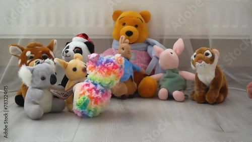 Stuffed and fluffy plush and rainbow toys sheep, unicorn and koala fall on the laminate flooring in the play area against the backdrop of other toys. Slow motion. photo