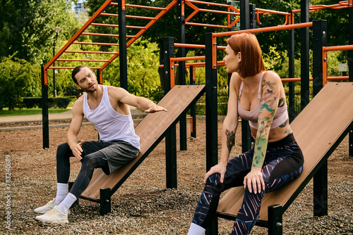 A man and a woman in sportswear sit on benches  exercising together in a park. Their determination and motivation are evident.