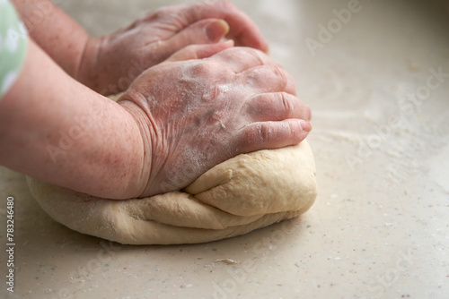 Elderly woman's hands knead dough on table. Copy space. © ROMAN DZIUBALO