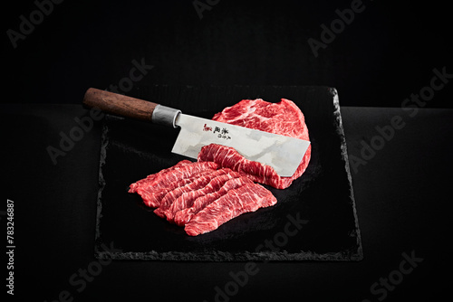 Wagyu beef slices with Japanese carving knife on black slate