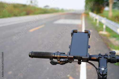 Smartphone and quick release holder attached on the handle bar of a bicycle with country road on background