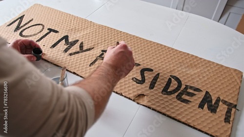Caucasian Male Preparing Banner for Political Demonstration Raid before Presidential Election with Not My President Text Painted on Cardboard