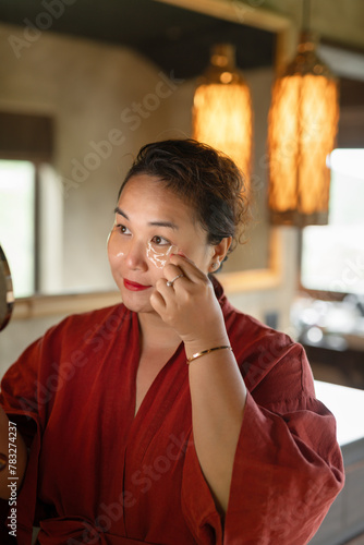 Plussize asian lady holding mirror and applying under eye photo