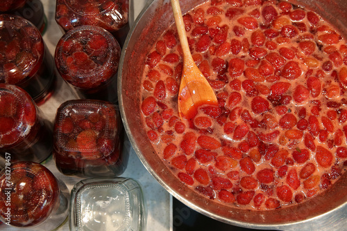 Cooking strawberry jam in a large bowl at home. Wooden spoon in a bowl with jam. Empty glass jam jars and jars filled with jam.