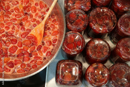 Cooking strawberry jam in a large bowl at home. Wooden spoon in a bowl with jam, glass jars filled with jam.