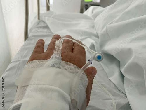 A hand with an IV line in a hospital receiving intravenous fluid. Close-up view captures medical care in a clinical setting. High quality photo
