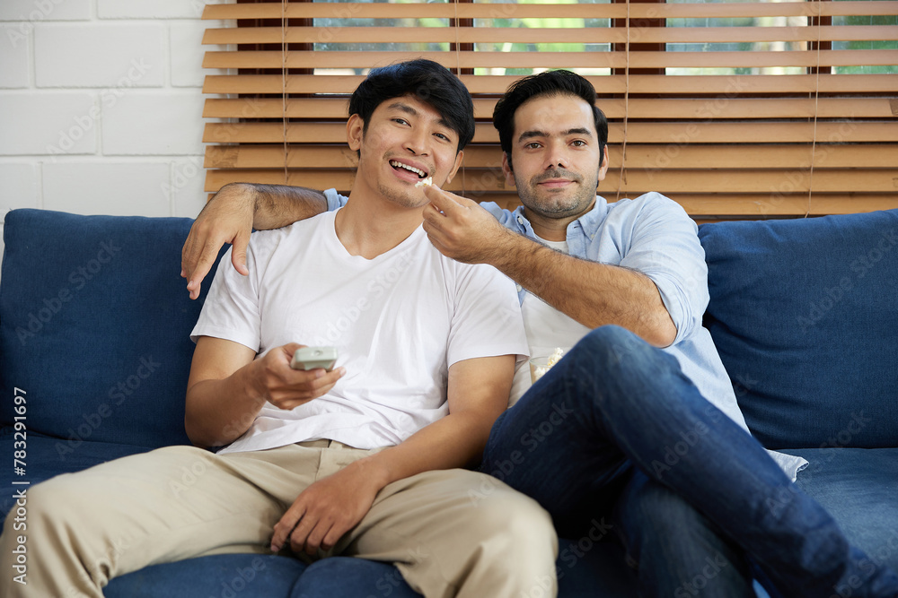 LGBT gay couple watching tv and eating popcorn in living room LGBT gay couple watching tv and eating popcorn in living room