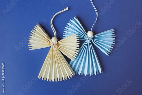 Two figures of festive angels made of paper laying on blue background