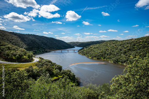 A beautiful nature view of the Tagus River valley from the Mirador Rio Tajo. Blue sky, white clouds, water, bridge and a floating boom. Monfrague National Park, Extremadura, Spain photo