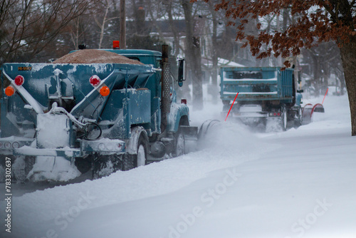Two snowplows clearing a road and dropping sand