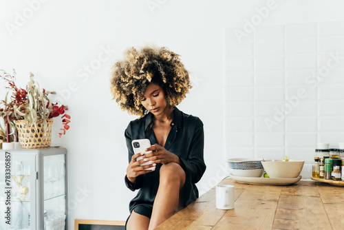 Young afro woman using smartphone in a modern kitchen photo