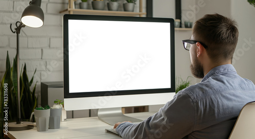A man is sitting in front of a blank white computer monitor, engaged in work.