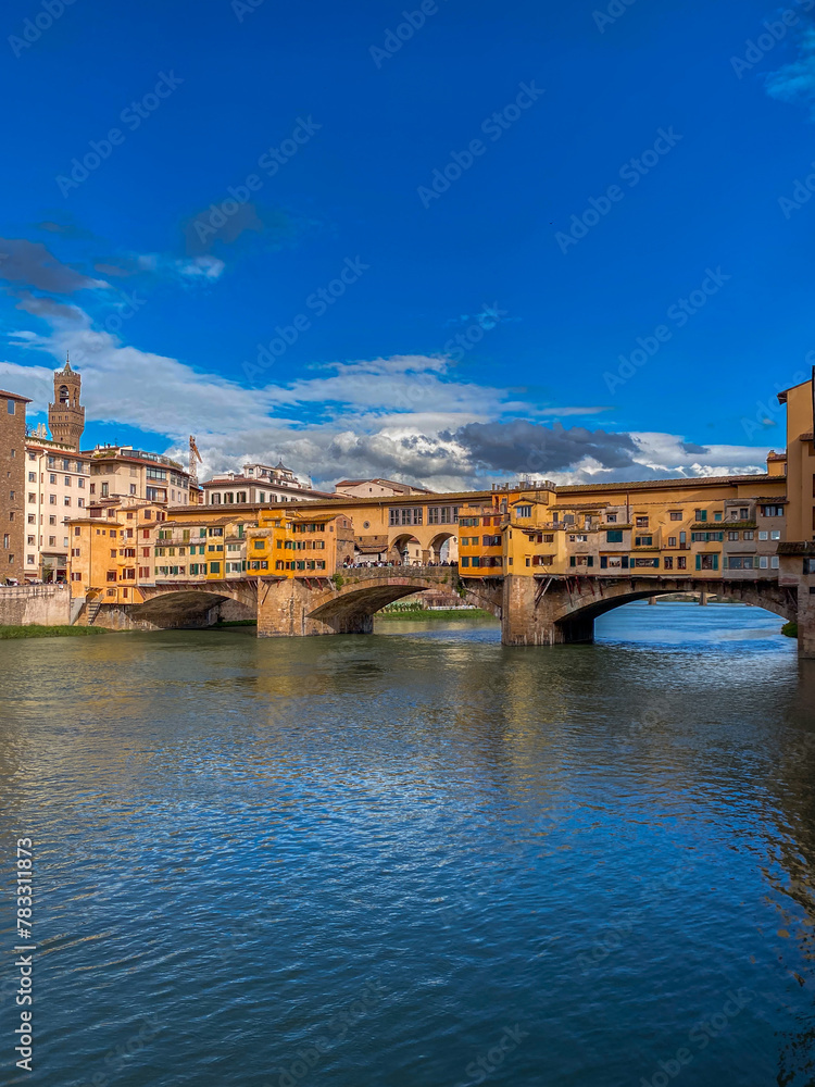 Ponte Vecchio bridge over the Arno River in Florence, Italy with blue sky reflecting on the river