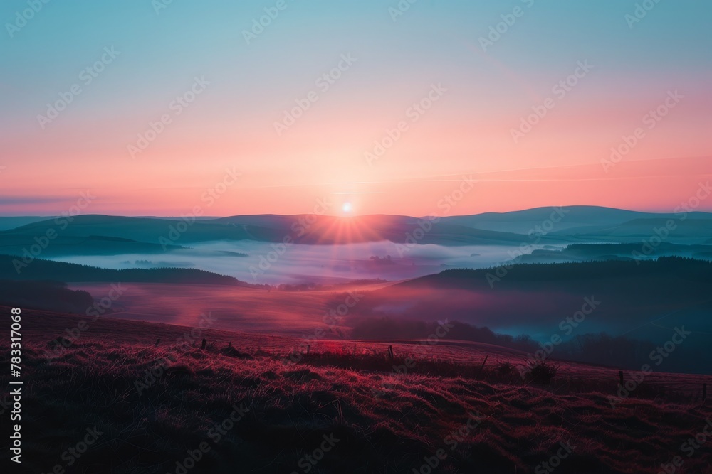 Breathtaking sunrise over misty hills with a vivid gradient of pink and blue hues, casting a serene glow on the undulating landscape.

