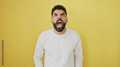 Frustrated young man screaming in a fit of rage, standing angry and furious, isolated on a yellow background, shouting with aggressive anger. photo