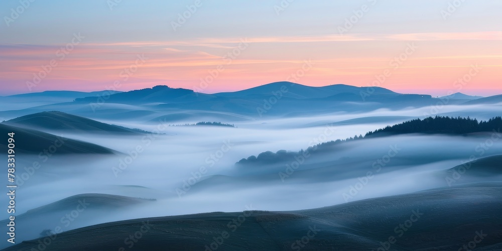 The sky is a beautiful shade of pink and orange. The mountains are covered in fog. The misty atmosphere gives the scene a serene and peaceful feeling