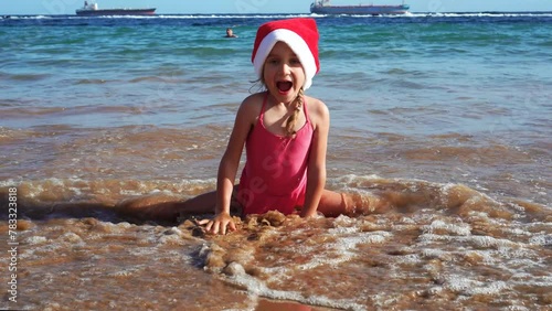 Children in Christmas hats are making sands towers on the beach. Xmas vacation. The wave suddenly hits the girl in the back. High quality 4k footage