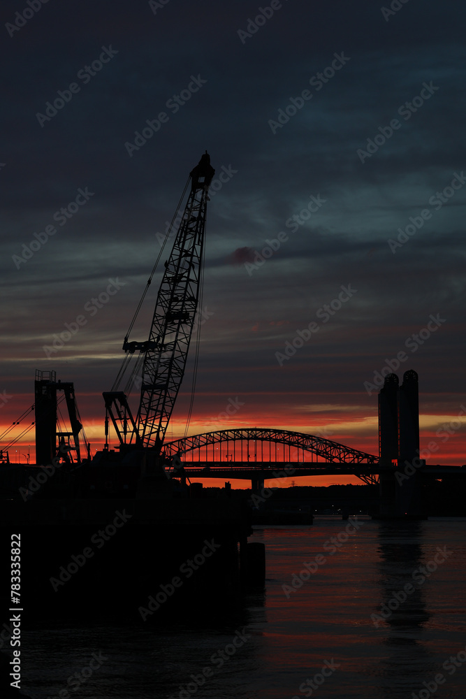 Obraz premium Silhouette of a crane and bridge during sunset