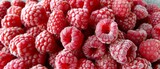   A red raspberry heap rests atop a white table, adjacent to another raspberry pile