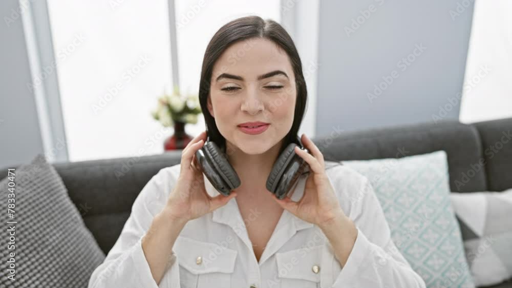 Smiling young hispanic woman enjoying music with headphones in a modern living room.