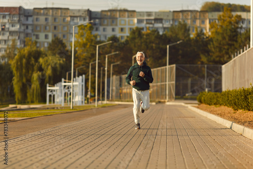 Mature sporty male runner jogging in city park. Healthy sporty fitness man running outdoors training for wellness  health and cardio. Workout in nature and healthy lifestyle concept.