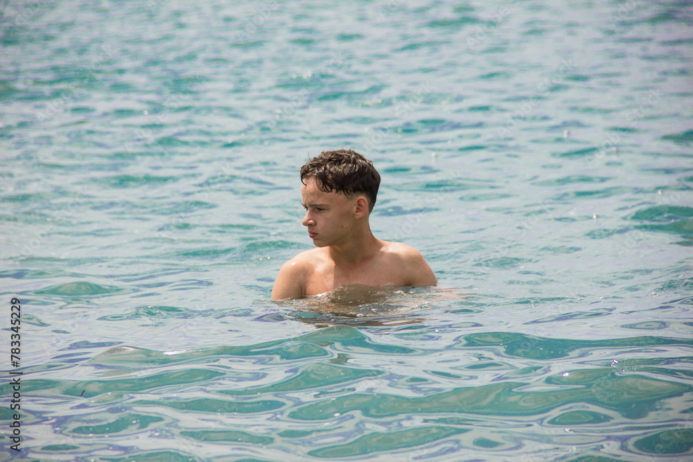 A young man stands in the water and looks into the distance.