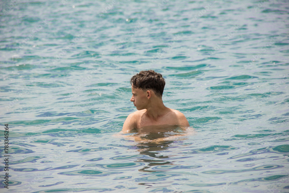A young man stands in the water and looks into the distance.