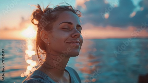 Young woman with eyes closed in bliss against a backdrop of a setting sun and shimmering ocean in warm hues of pink, orange, and blue, evoking tranquility and serenity.