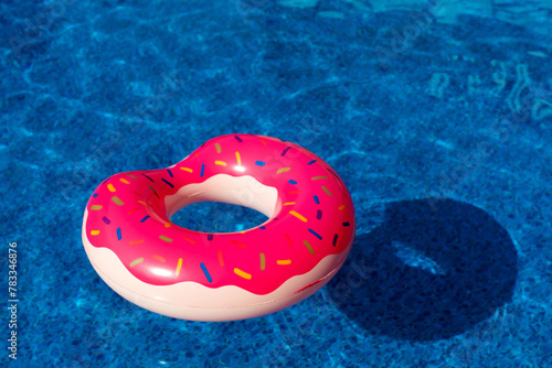 Pink inflatable ring in the water of a swimming pool on a sunny day. Summer holiday concept. Donut shaped inflatable ring