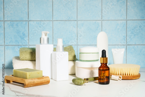 Natural cosmetic products in the bathroom, blue background. Soap, mask, face cream, serum bottle, jade roller.