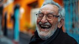 An elderly man with glasses laughing contagiously on a colorful urban street, radiating warmth and happiness. World Laughter Day.