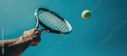 Tennis player is holding racquet and hitting ball on blue background