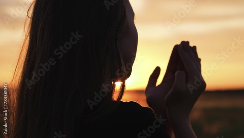 Woman praying with folded hands at sunset silhouette. Religious pious orthodox christian spiritual believing faithful girl at morning dawn sunrise reading prayer bible turning to god jesus christ.