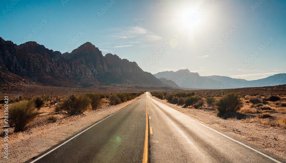 desolate desert road with mountains with sunflare western united stated