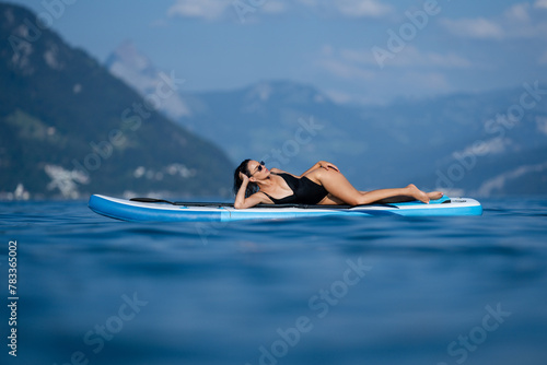 Beautiful young woman relaxing on paddle board in the summer lake or sea water. Luxury summer resort. Sexy sensual fit woman with slim body rest in water. Beautiful model enjoying summer travel.