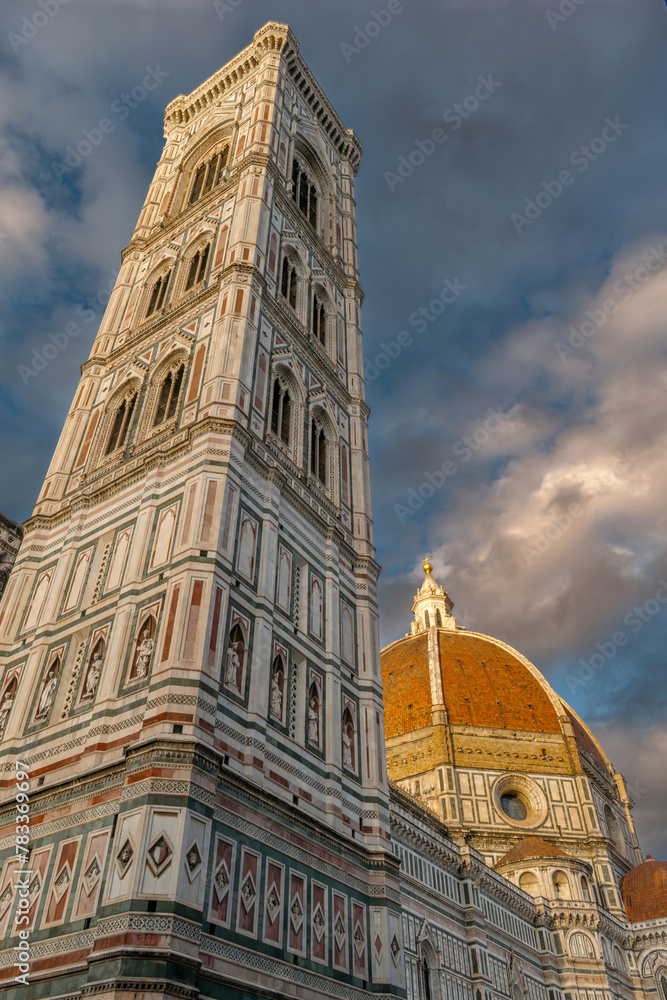 Obraz premium Florence, Italy - Giotto Campanile bell tower viewed with the dome of the Cathedral of Santa Maria del Fiore in Piazza del Duomo with warm sunset light on pictorial sky with clouds