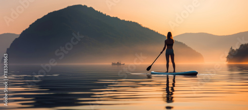Silhouette of a young woman paddleboarding on the serene sea at sunset, blending fitness with relaxation.